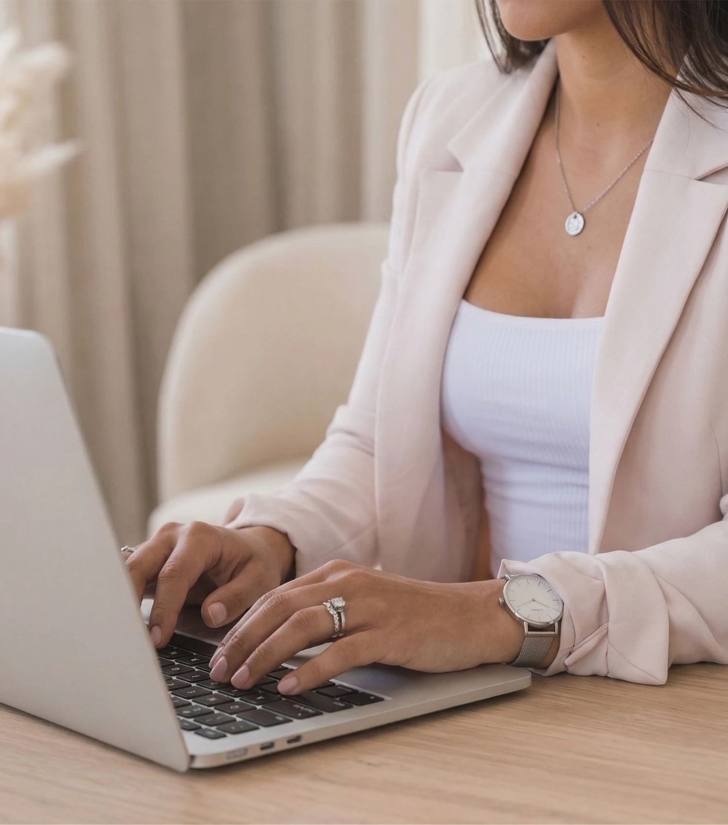 A woman in a pink blazer types on a laptop at a wooden desk, representing online course website design Australia, face unseen.