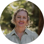 Jane Smiling woman in light green blouse, red lipstick, Brand and Web Design Gold Coast, outdoors with trees blurred in background.
