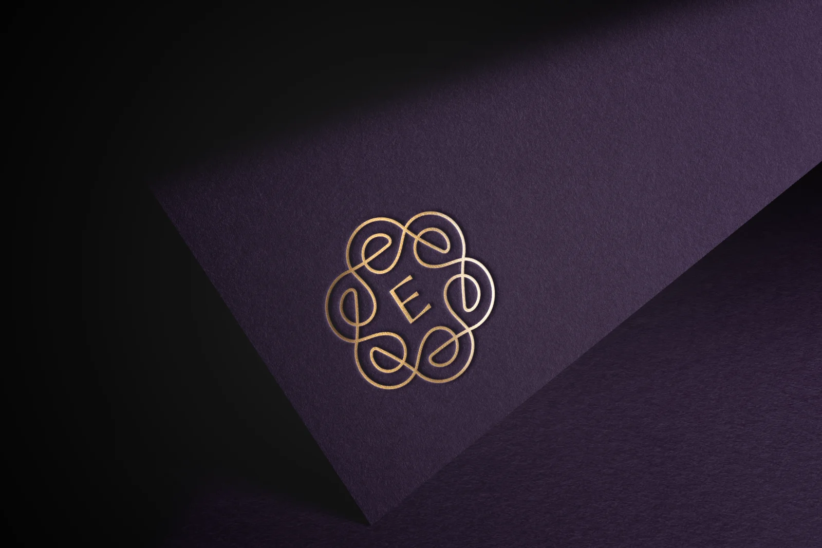 A gold ornate logo with an elegant, looping design surrounds the letter "E," embossed on a dark purple textured surface. A gold ornate logo with an elegant, looping design surrounds the letter "E," embossed on a dark purple textured surface.